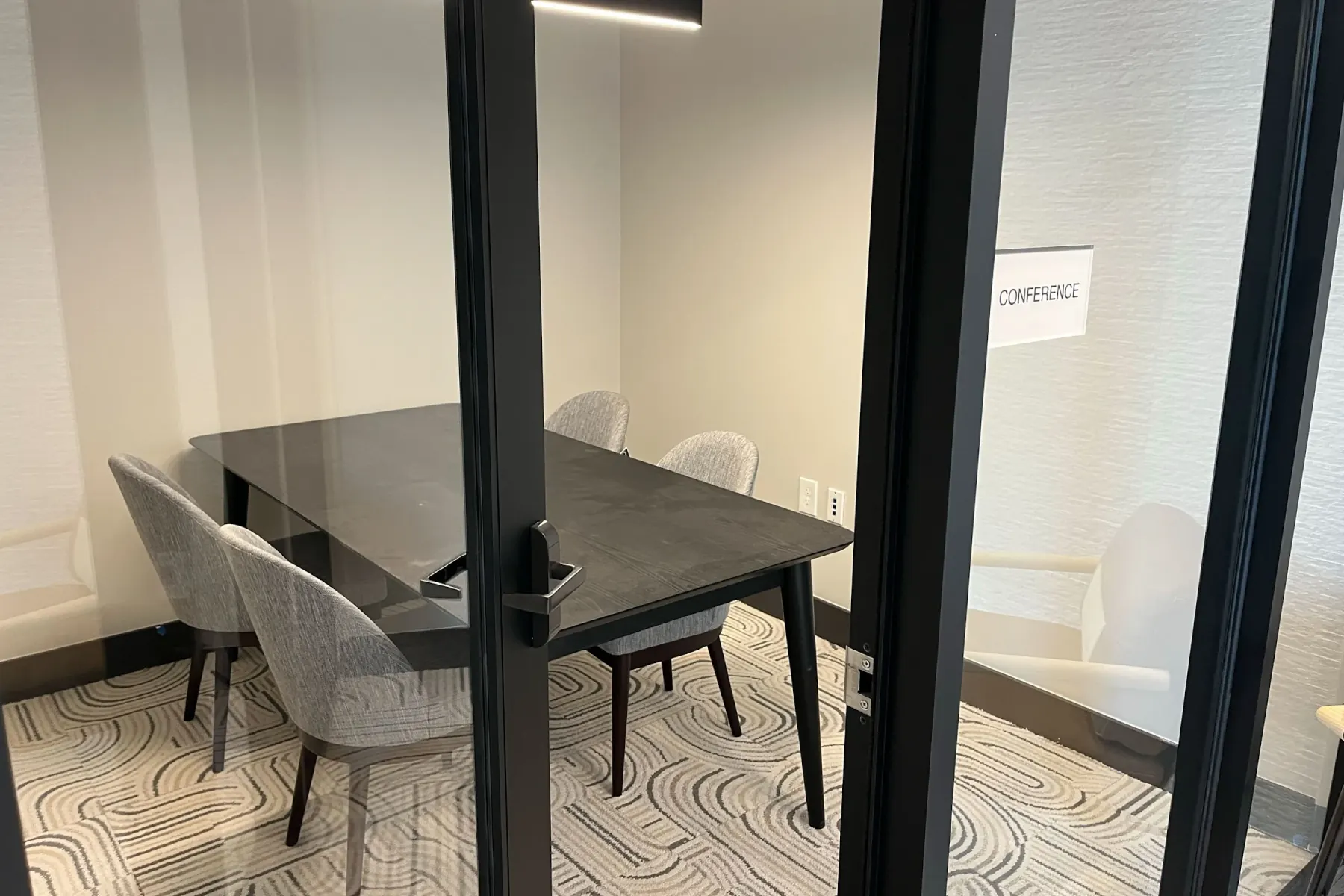Glass-enclosed conference room with dark wood table and upholstered chairs