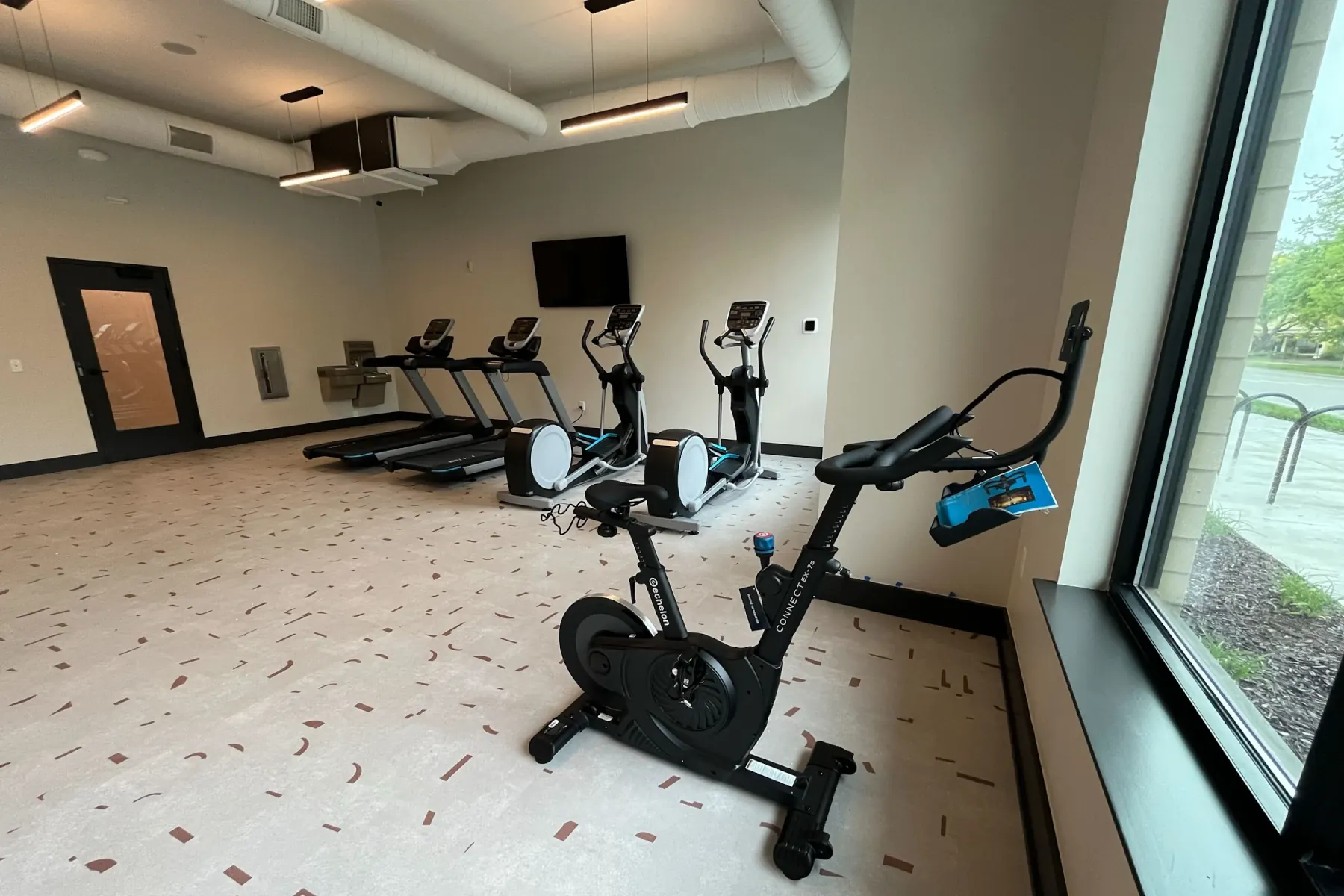 Packard Row fitness center with treadmills, ellipticals, and an Echelon connected bike near a window with natural light