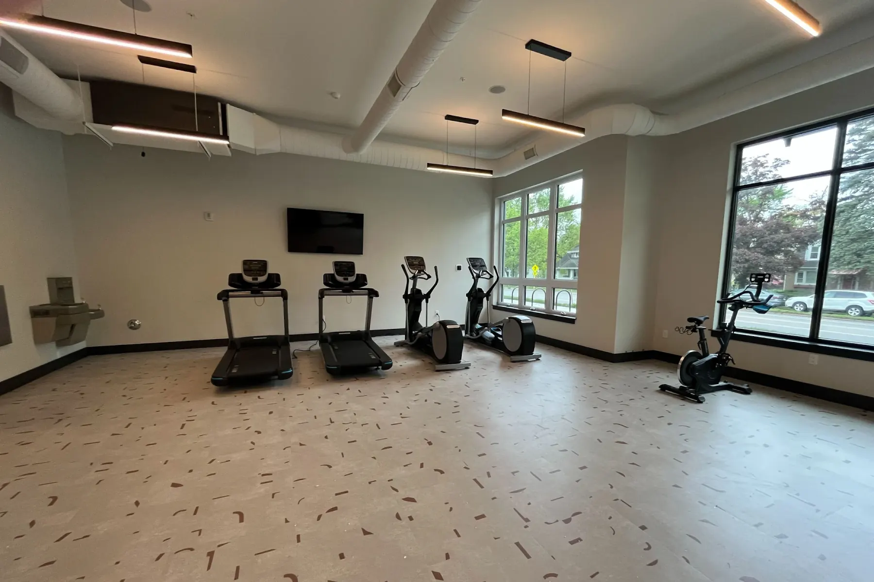 Wide view of Packard Row's fitness center with treadmills, ellipticals, a stationary bike, and a wall-mounted TV